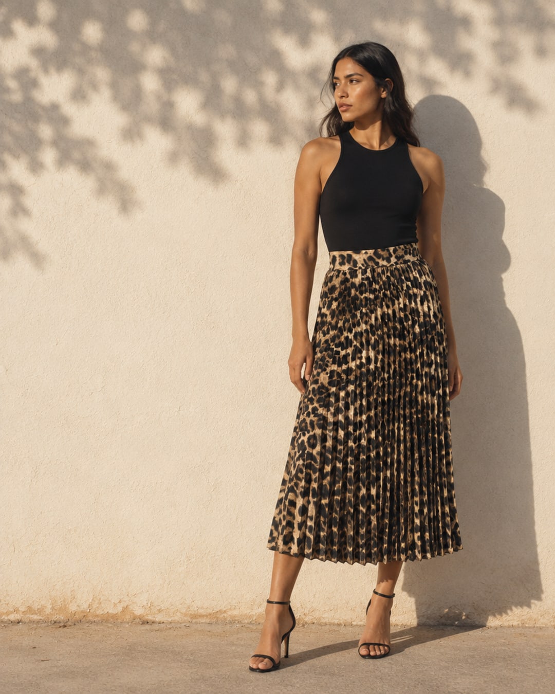 Campaña: la falda plisada de leopardo con top negro, contra un muro al sol con la sombra de un árbol.